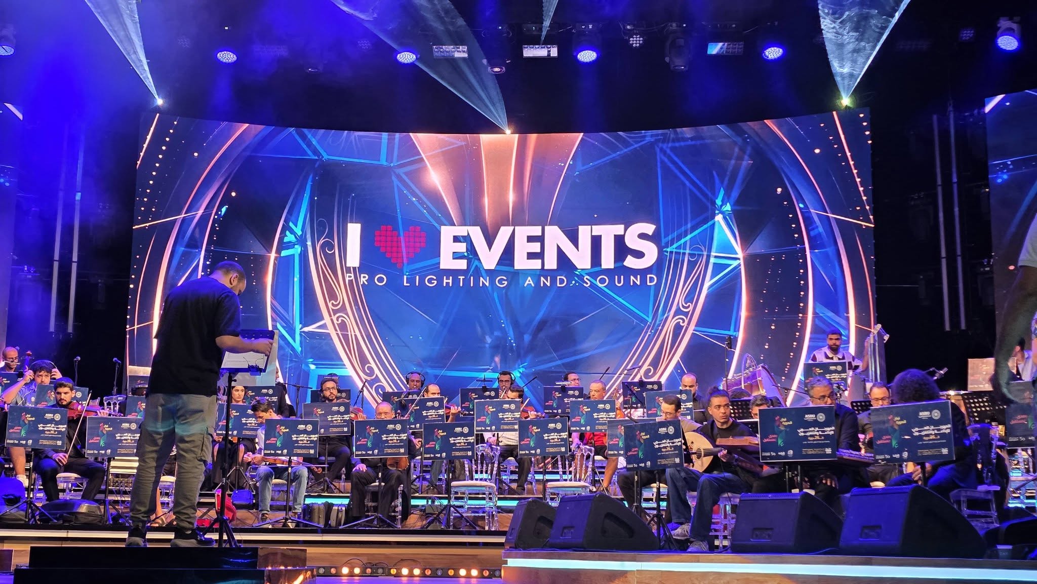 موسيقيون على الخشبة أمام جدار شاشات I Love Events